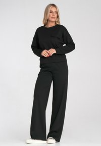 Czarna bluza z kapturem z przednią kieszenią, zestawiona z luźnymi czarnymi spodniami. Tkanina wydaje się miękka o gładkiej fakturze. Casualowy design.