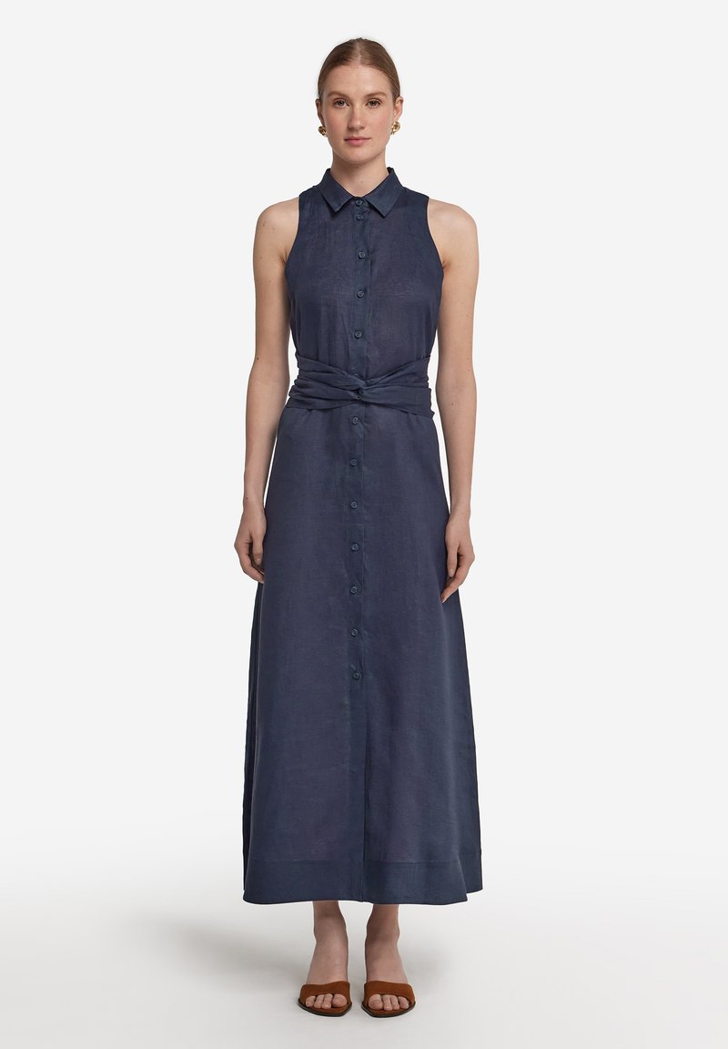 Ärmlös, marinblå linniklänning med knappstängning, krage och knytdetalj i midjan. Maxilängd med en mjuk textur och en flödande silhuett.