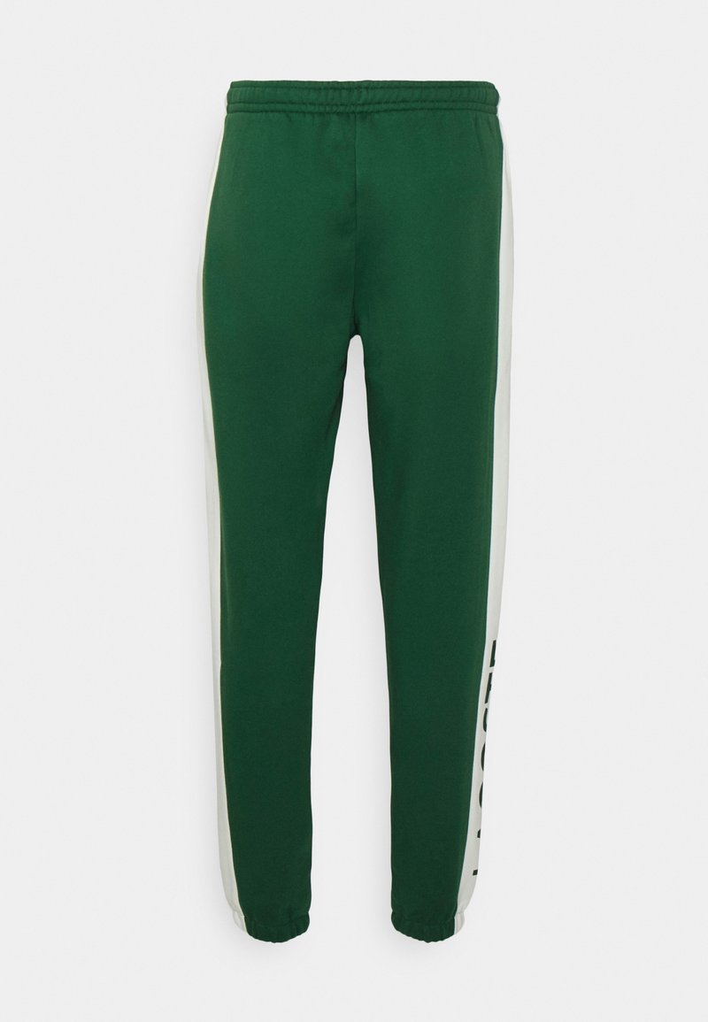 Pantaloni sportivi verde scuro con strisce laterali bianche e polsini elasticizzati, presentati su uno sfondo bianco.