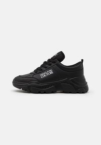 Zapatillas negras con suela gruesa y parte superior texturizada. Presenta cordones, un cuello acolchado y un logo impreso en el lateral.