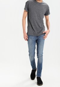 Camiseta gris de manga corta, jeans ajustados azules y zapatos negros. La camiseta de algodón tiene un acabado texturizado, y los jeans presentan un aspecto desgastado.