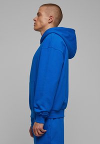 Blå sweatshirt med hætte, lavet af bomuldsblandet stof. Har ribbede manchetter, kængurulomme og en afslappet pasform.