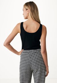 Czarny bezrękawnik z okrągłym dekoltem połączony z wzorzystymi spodniami o wysokim stanie, które mają czarno-białą geometryczną kompozycję.
