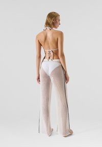 White crochet cover-up pants with a loose fit, featuring a black side stripe, paired with a white bikini top. Smooth, lightweight texture.