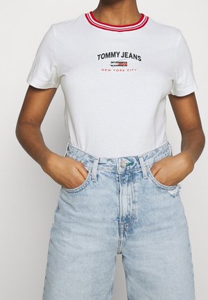 Hvid bomulds-T-shirt med rødt, stribet krave; har "TOMMY JEANS" og "NEW YORK CITY" trykt i sort og rød. Kombineret med lyseblå jeans.