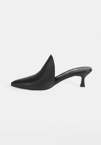 Mules en cuir noir avec un bout pointu, un dos ouvert et un petit talon incliné ; texture lisse avec des éléments de design minimalistes.