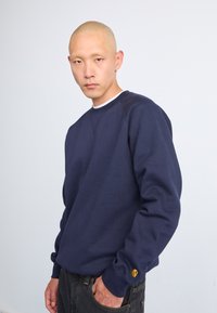 Marineblauwe sweatshirt gemaakt van textuurstof; heeft een ronde halslijn en ribgebreide manchetten, met een klein logoaccent op de linkermouw.