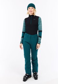 Turquoise skibroek met een zwarte rits-top met turquoise patroon op de mouwen. Draagt het met zwarte skischoenen en een turquoise gebreide muts.