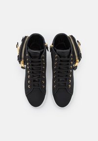 Svarta högskopade sneakers med guldfärgade ögla och dragkedjor, med ett slätt tygovre och vit gummisula.