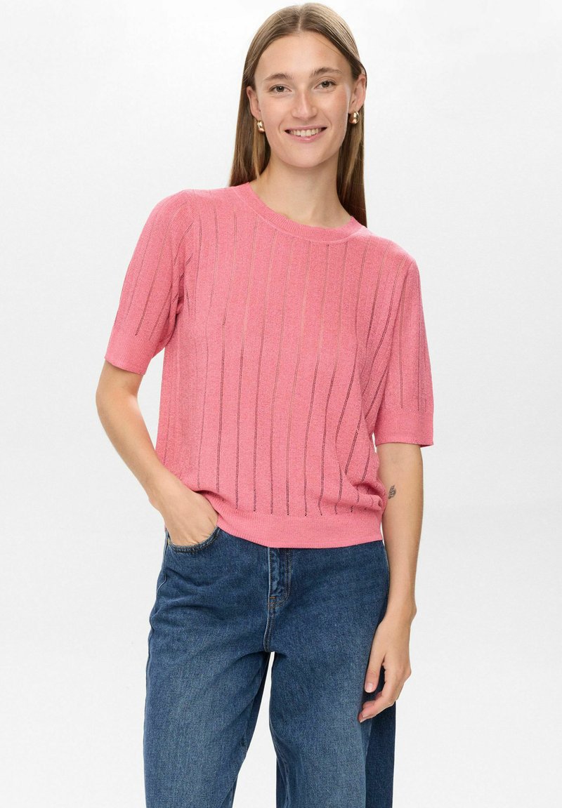 Ljusrosa kortärmad tröja med vertikal ribbtextur. Mjukt tyg, rund halsringning och avslappnad passform, kombinerat med mörkblå jeans.