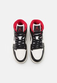 Czarno-białe sneakersy wysokie z czerwonymi akcentami, z perforowaną częścią na palce, czarnymi sznurówkami i logo Jordana na języku.