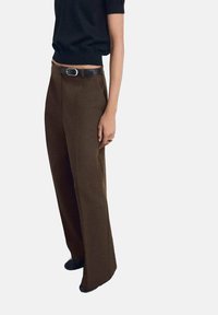 Pantalones de pierna ancha en tejido marrón oscuro con una textura suave, que presentan un cinturón negro con una hebilla plateada, combinados con una blusa negra ajustada.