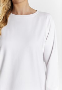 Cămașă albă cu mâneci lungi, realizată dintr-un material moale, cu guler rotund și mâneci raglan. Textură netedă, fără modele sau accente vizibile.