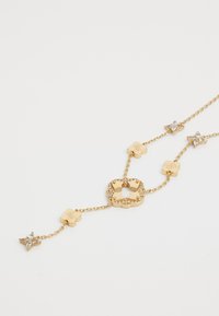 Gouden ketting met bloemvormige schakels, Swarovski kristal accenten en een centrale bloempendant versierd met stenen.