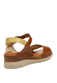 Sandalia de cuero marrón con acento amarillo, diseño de tiras cruzadas, punta abierta y plantilla acolchada. Presenta una suela de cuña marrón texturizada.