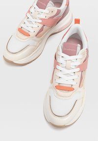 Baskets blanches et pêche avec une tige en mesh et synthétique, bout rond, design à lacets, avec des accents texturés et une sangle rose.