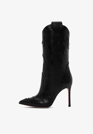 Botín de cuero negro de tacón alto con punta afilada y patrones decorativos perforados, que presenta una silueta ajustada y un tacón de aguja.