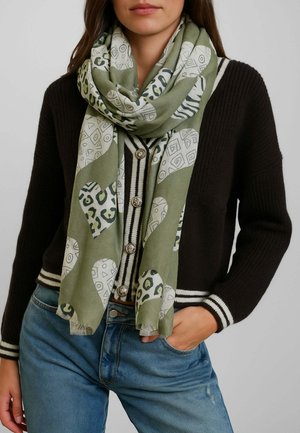 Sciarpa verde a motivo geometrico e leopardato, realizzata in tessuto morbido, avvolta attorno al collo e abbinata a un cardigan scuro.