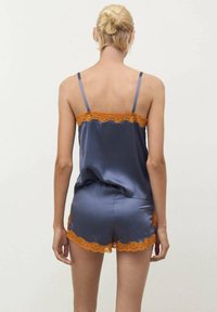 Pigiama in satin blu navy con bordi in pizzo arancione. Presenta una canotta con spalline sottili e pantaloni corti coordinati con bordi a forma di scallop.
