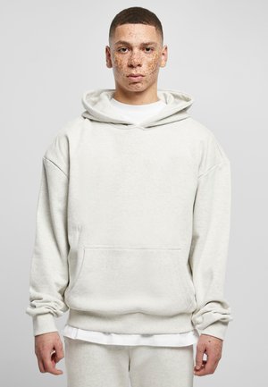 Light gray hoodie made of soft fabric, featuring a front pocket, loose fit, and a large drawstring hood. Layered over a white T-shirt.