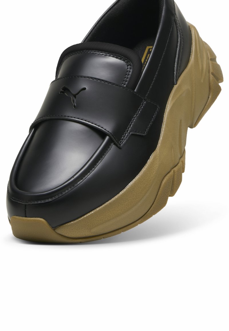 Czarne skórzane buty typu slip-on z fakturowaną, tanową gumową podeszwą. Posiadają przeszywaną panel i logotyp na górnym pasku. Okrąły czubek.