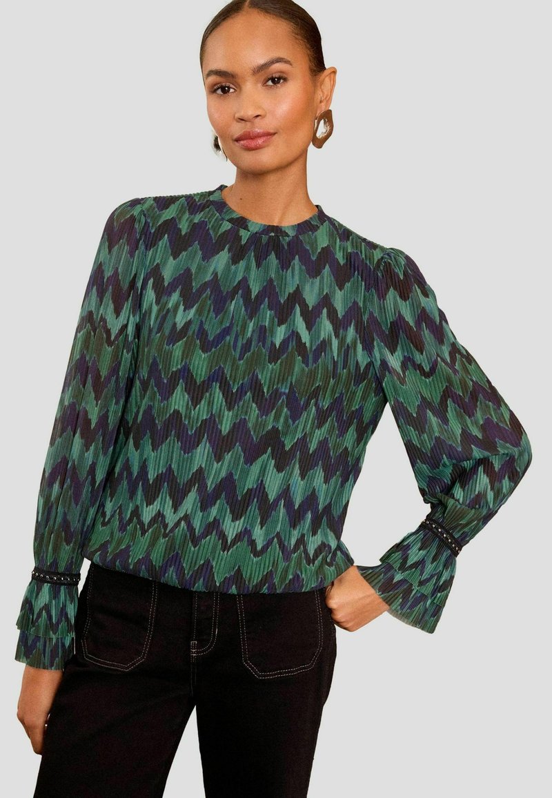 Bluza z dolgimi rokavi z zigzag vzorcem v zeleni in mornarsko modri barvi, z nabranim teksturo, okroglo ovratnico in volančki na koncu rokavov, okrašenimi z črnimi biseri.