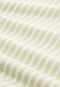 Hellgrüner Stoff mit weißen wellenförmigen Streifen und eingeschnittenen Details, der eine glatte Textur und ein weiches, dezentes Muster zeigt.