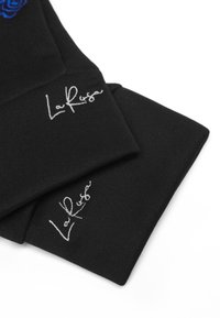 Svart tygföremål med broderad text "La Rasa" i vitt. Designen har en texturerad finish med en enkel, minimalistisk stil.