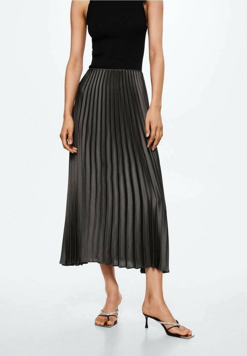 Falda midi negra plisada con textura suave, cintura alta y silueta fluida, combinada con sandalias de tacón con tiras.