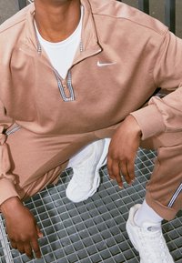 Nike zip-up sweatshirt i beige med svart-vita rutiga accenter, matchad med vita skor. Har en mjuk textur och avslappnad passform.