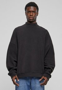 Svart oversized sweatshirt med høy krage, ribbede mansjetter og en glatt tekstur. Kombinert med blå denimjeans. Enkel, minimalistisk design.