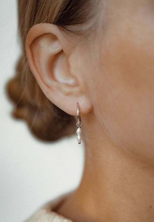 Pendientes de aro de plata que cuentan con dos perlas blancas y un pequeño acento metálico, exhibiendo un acabado suave y pulido.