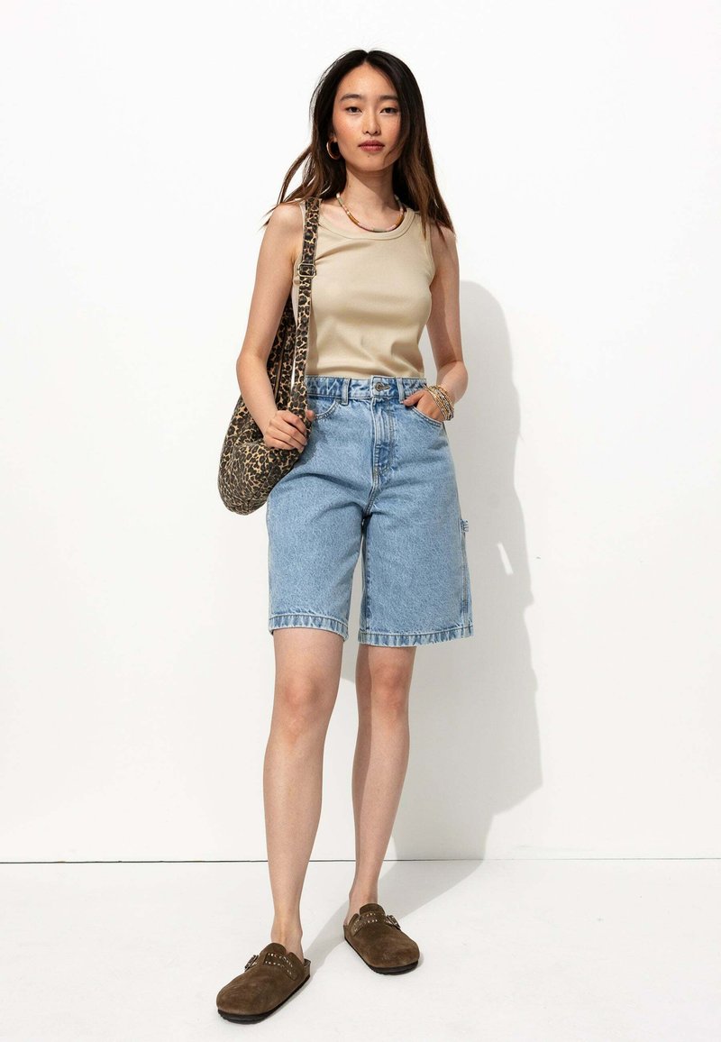 Débardeur beige, shorts en denim bleu avec des bords effilochés, chaussures slip-on en daim marron, et un sac en imprimé léopard. Design simple et décontracté.