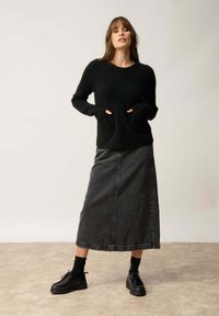 Pull en maille noir avec une finition texturée et des poches avant, associé à une longue jupe en denim grise et des chaussures noires à lacets.