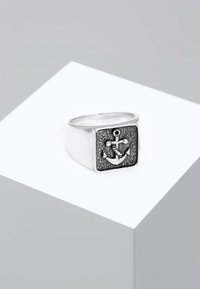 Sølv firkantet ring med et tekstureret sort ankerdesign og en lille rund accent, sat mod en glat poleret ring.