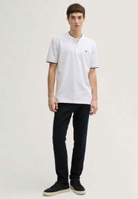 Tricou alb cu garnitură neagră, mâneci scurte și guler cu nasturi, purtat împreună cu pantaloni negri slim-fit și adidași negri.