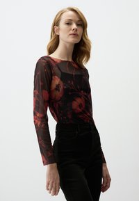 Haut noir transparent à manches longues avec un motif floral rouge, encolure ronde et design ajusté, associé à un pantalon noir taille haute.