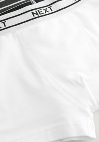 Boxers en coton blancs avec une ceinture rayée noir et blanc marquée "NEXT". Présente une texture lisse et des détails de couture subtils.