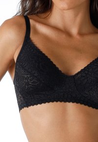 Bralette in pizzo nero con design morbido e senza fodera, bordi scallopati e spalline regolabili, che mette in risalto motivi floreali e una texture liscia.