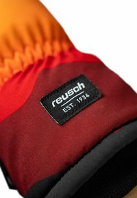 Rote und orange Handschuhe mit glatter Textur, versehen mit einem schwarzen Etikett mit weißem Text "reusch" und "EST. 1934" zur Markenidentifikation.