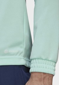 Hellmintgrüne Sportjacke aus strukturiertem Stoff, mit enganliegenden Bündchen und einem AEROREADY-Logo nahe dem Saum. Verfügt über ein lockeres Design.