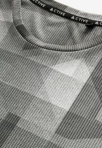 Grå træningsshirt med et struktureret mønster, med rund hals og et sort mærke med "ACTIVE" trykt på.