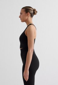 Melns sporta krūšturis un augsta vidukļa legingi, pieguļošs dizains, gluda tekstūra, minimāli šuves, īss garums ar izgriezumu detalizācijā.