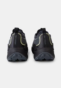 Black outdoor sneakers with a textured rubber sole, curved design, and reflective yellow accents on the upper. Features pull tabs at the back.