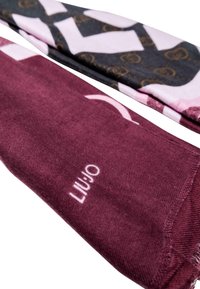 Due paia di calze: una bordeaux con logo bianco, l'altra decorata con motivi in nero, rosa e dettagli dorati. Misto cotone, texture a costine.