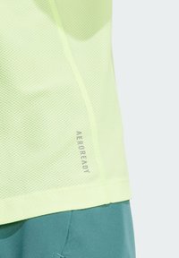 Camiseta deportiva de malla color amarillo claro con una superficie texturizada y un pequeño logo "AEROREADY" en la costura lateral. Diseño transpirable y ligero.