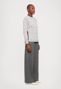 Light gray knitted sweater with a textured cable pattern, paired with dark gray wide-leg trousers. Sweater has a crew neckline and side slits.