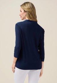 Navy blue, long-sleeve top with a rounded neckline and soft texture. Features a relaxed fit and a hem that extends below the hips.