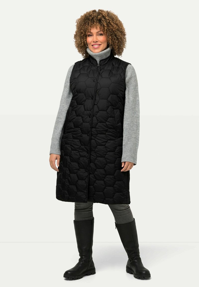 Schwarz, hexagonal gestepptes langes Weste mit hohem Kragen, kombiniert mit einem grauen Rollkragenpullover, grauen Leggings und schwarzen kniehohen Stiefeln.