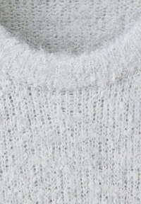 Gros plan sur un tissu tricoté doux, gris clair et duveteux montrant la texture et le motif côtelé du col d'un pull.